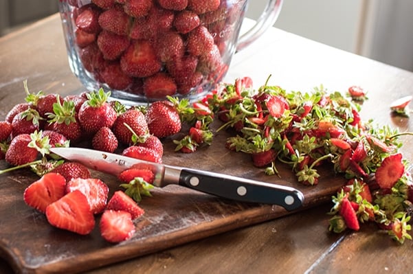 strawberries being hulled and sliced on a wooden cutting board