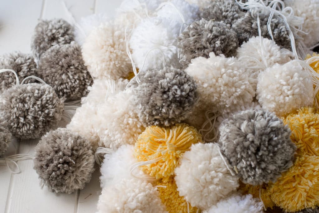 pile of grey, yellow, white and cream pom poms stacked on a white plank table.