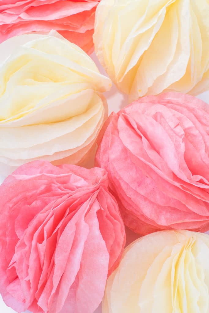 Pink and coral coffee filter paper pom poms on a bright white table