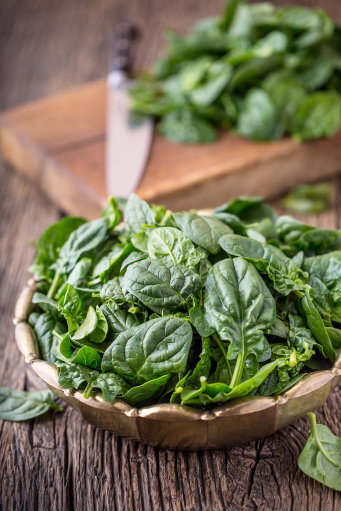 A wooden bowl on a rustic wooden table filled with ripe dark green lettuce freshly picked from the garden
