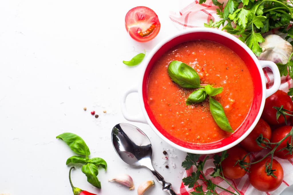 A bowl of tomato basil soup with sprigs of fresh basil. 