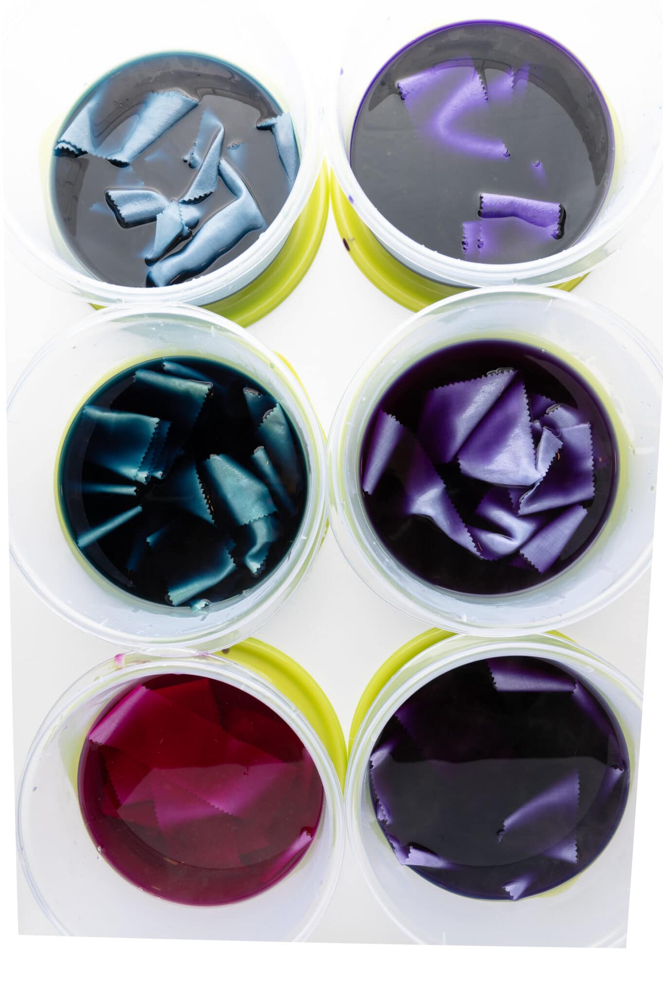 Test strips of fabric soaking in several containers of natural dye. Each container has. adifferent hue due to the use of mordants.