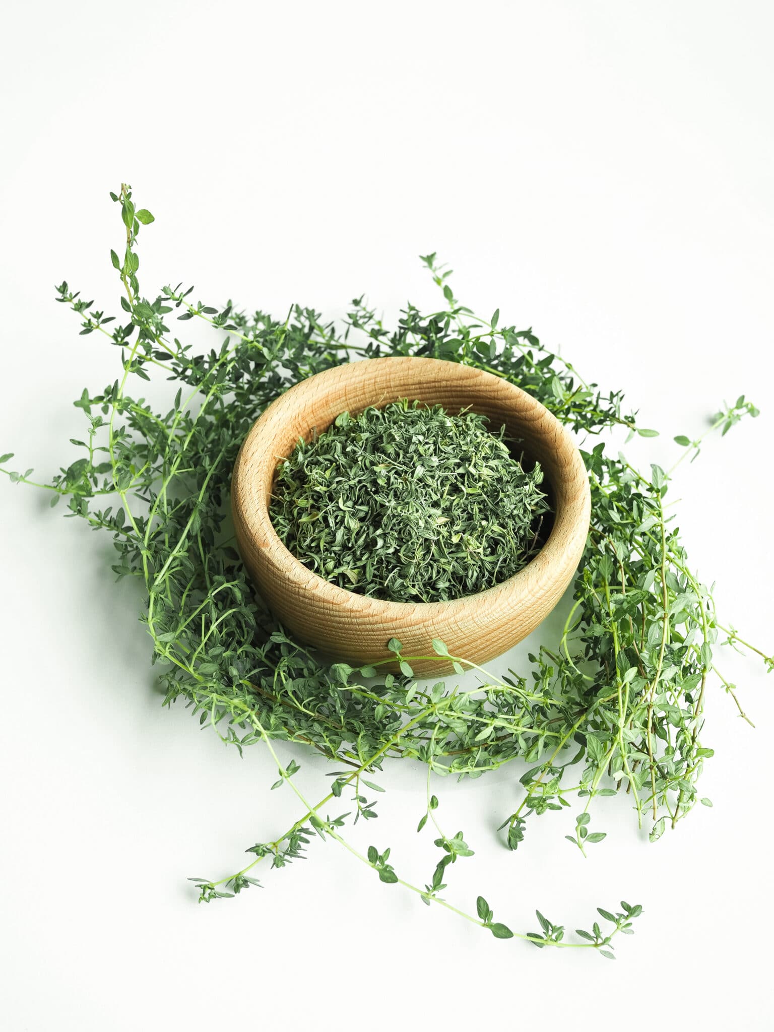 Wooden bowl of dry thyme on white background.