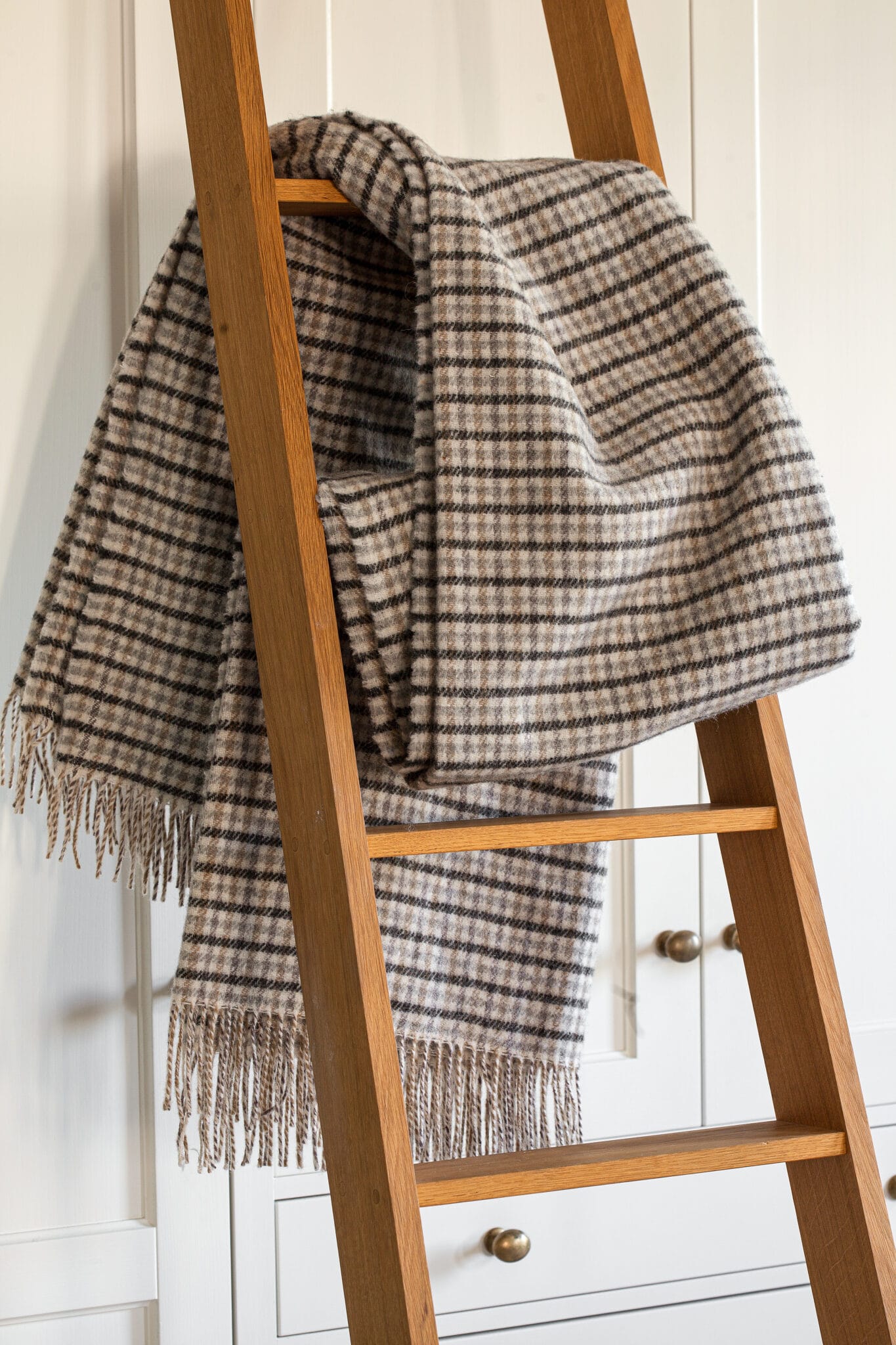 A blanket ladder with a throw blanket draped over a rung.
