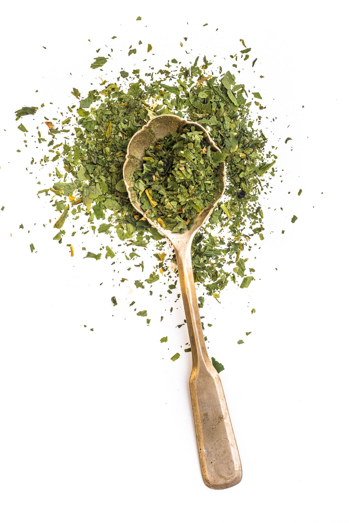 Dried basil on an antique golden spoon against a bright white background.