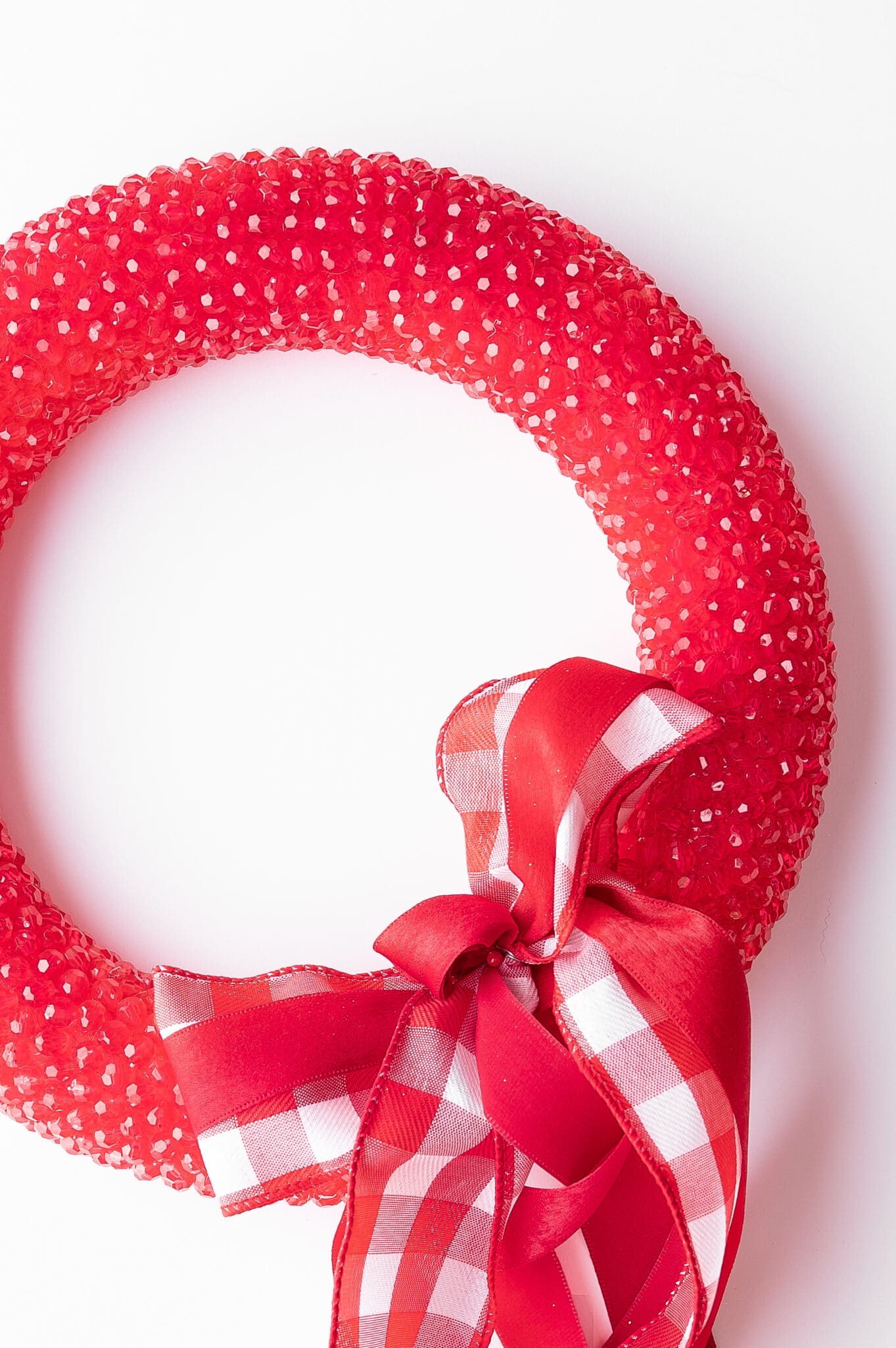 red Beaded wreath with a big red gingham bow against a bright white background. 