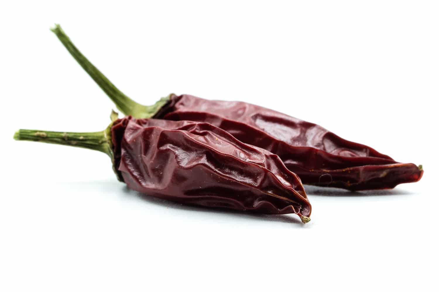 two deep red dried jalapeno peppers against a bright white background. 