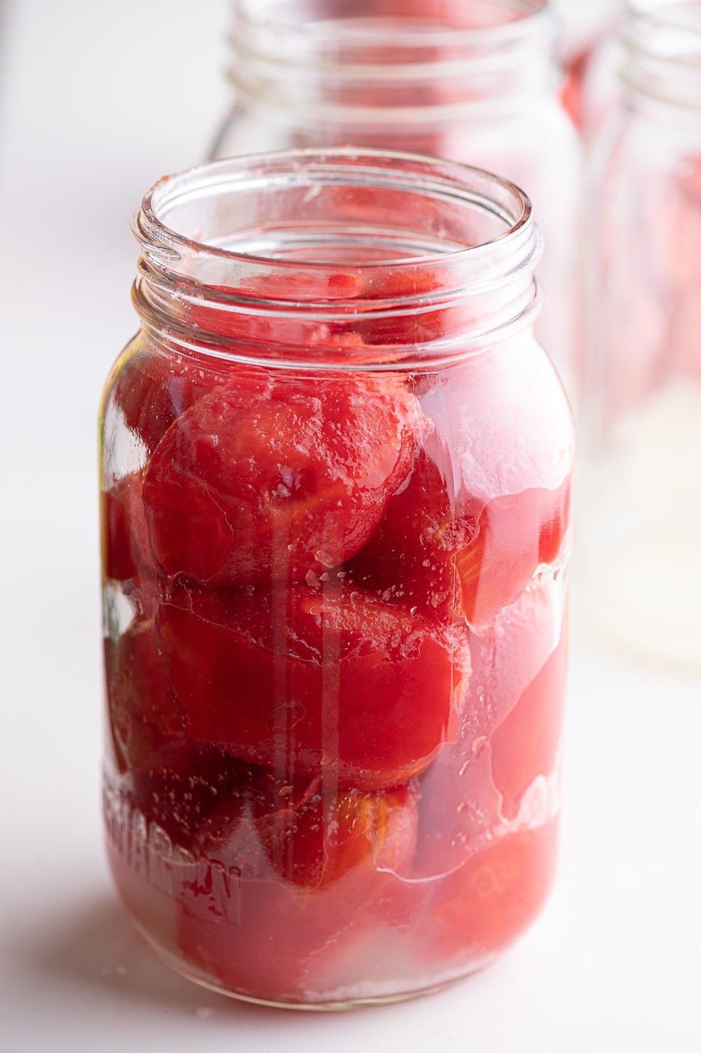 Canning whole tomatoes into a clean mason jar.