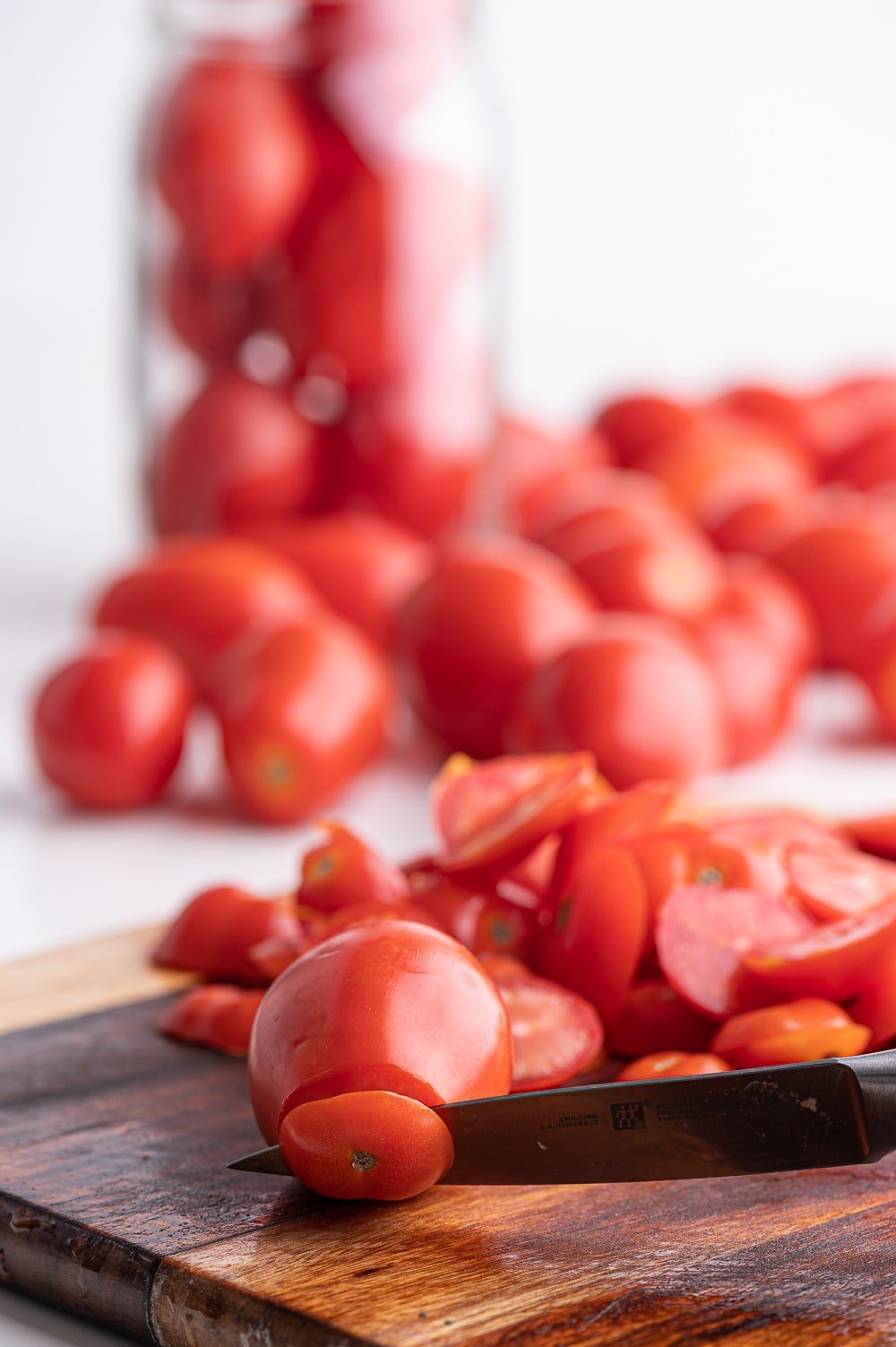 A rustic cutting board with paste tomatoes having the blossom end cut off with a paring knife.