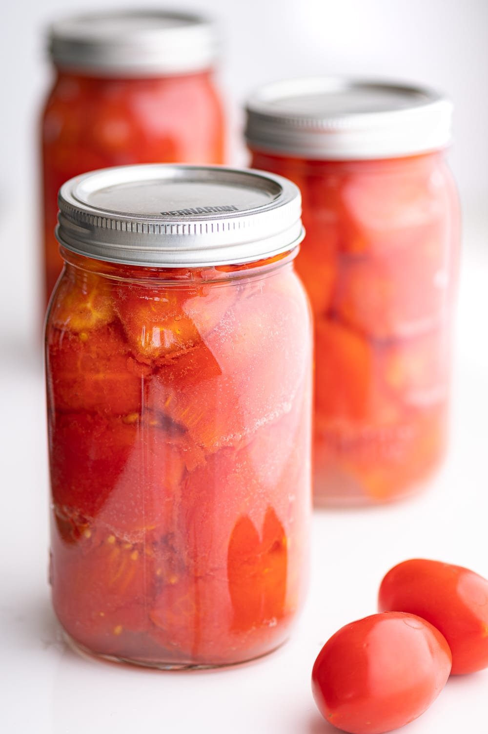 Three jars of canned whole tomatoes against a bright white background.