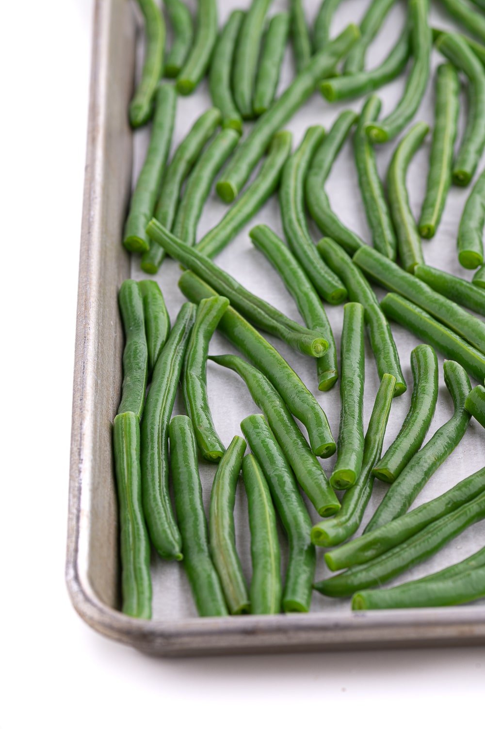 Dried string beans resting in a single layer on a parchment lined baking sheet.