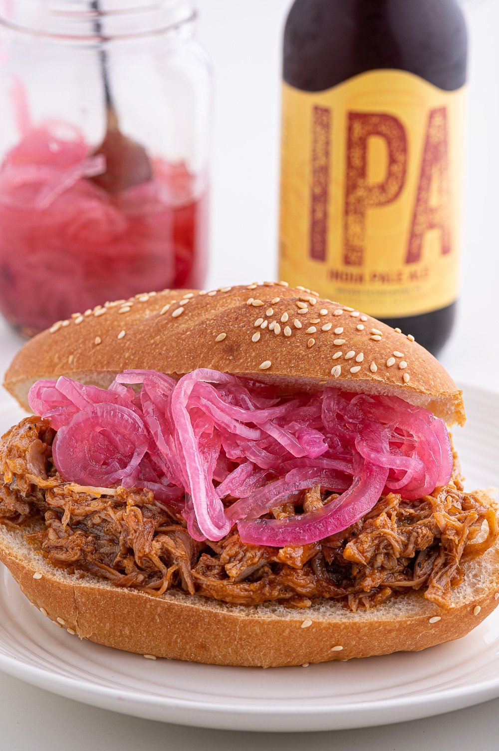 Pickled red onions on top of piled pulled pork on a fresh sesame seed roll.
