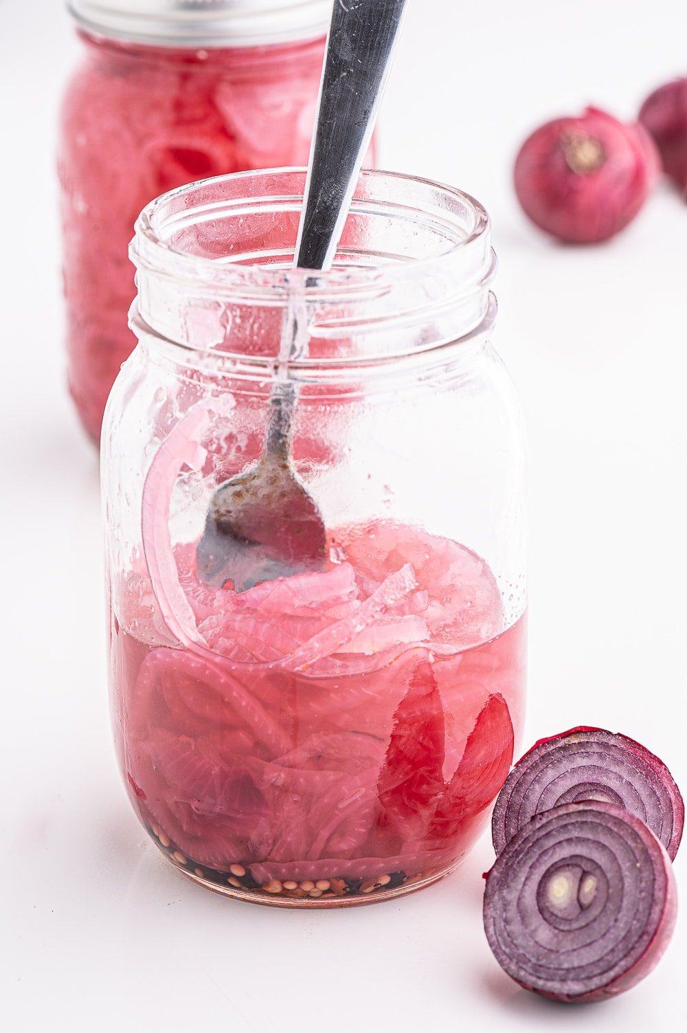 A half filled open jar of red pickled onions on a bright white background.