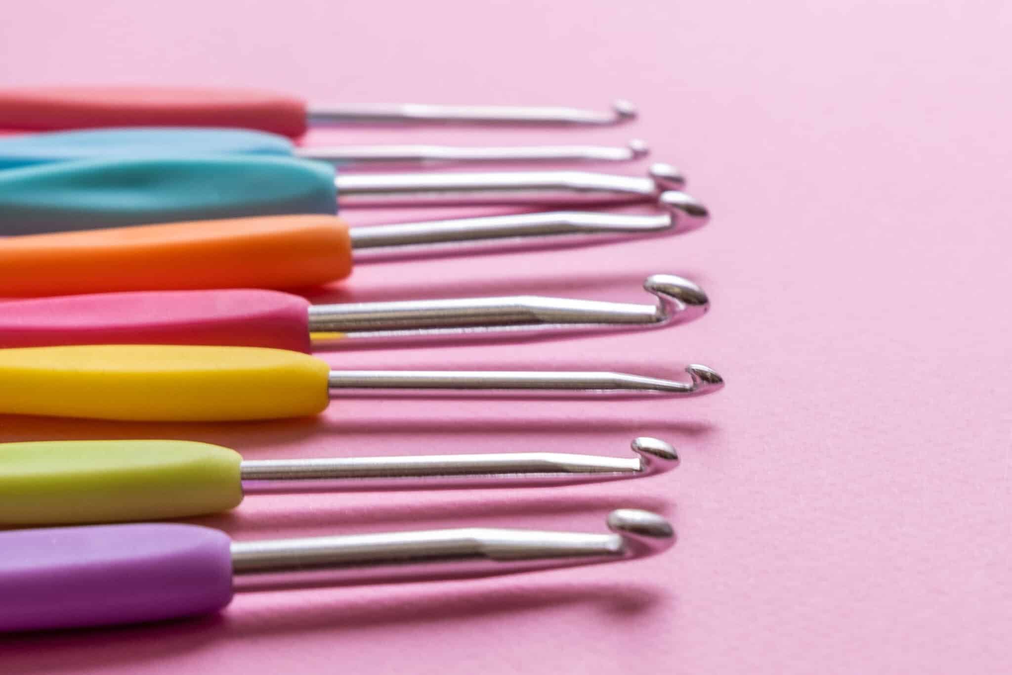 Closeup image of different size colorful crochet hooks on soft pink background with copy space,