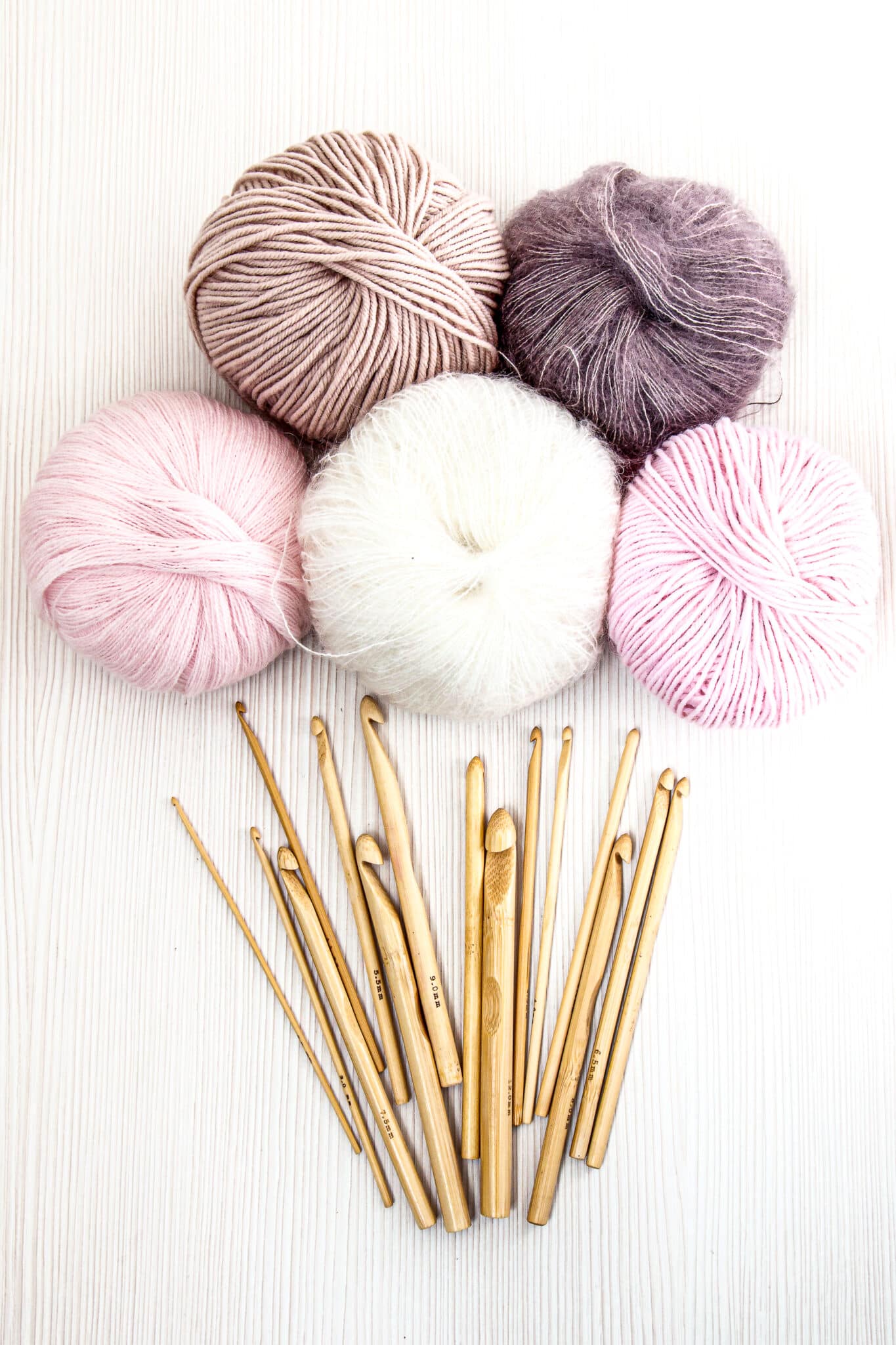 Wooden crochet hooks on white wood background with balls of yarn pastel colors. Top view. Hobby and handmade concept..