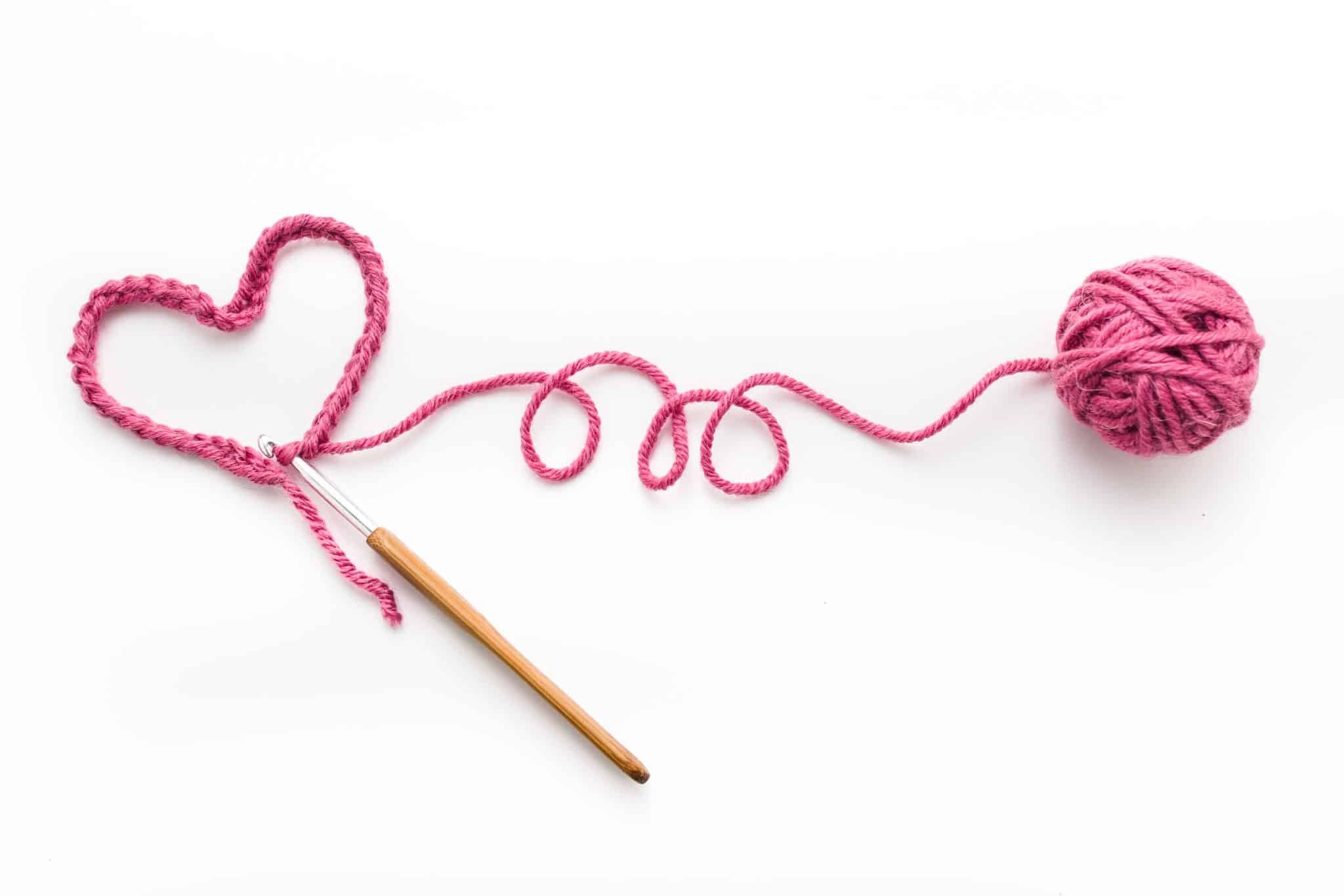 A small crochet heart with hook and ball of yarn against a bright white table top.