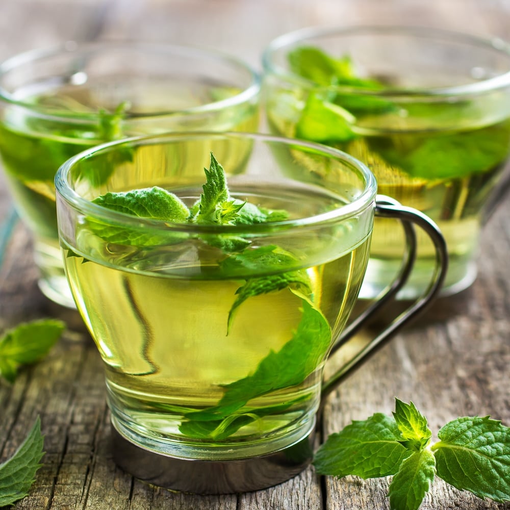 Hot mint tea in glass cup on wooden background.